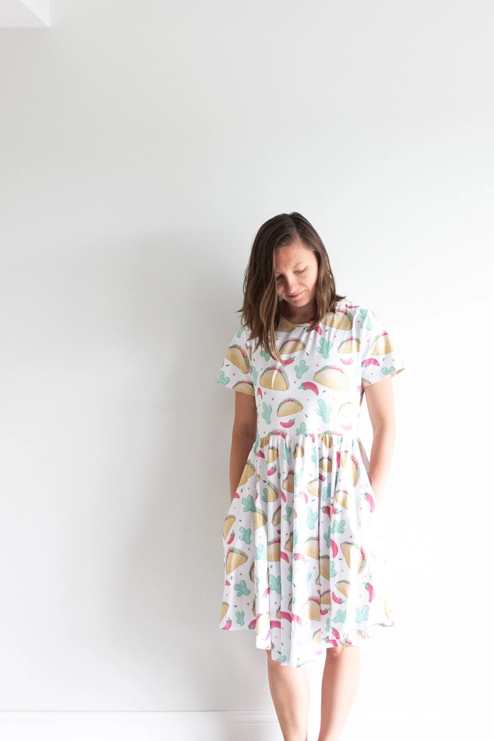 Woman posing with hands in the pockets of a white dress with pattern of tacos, chili peppers, and cacti.