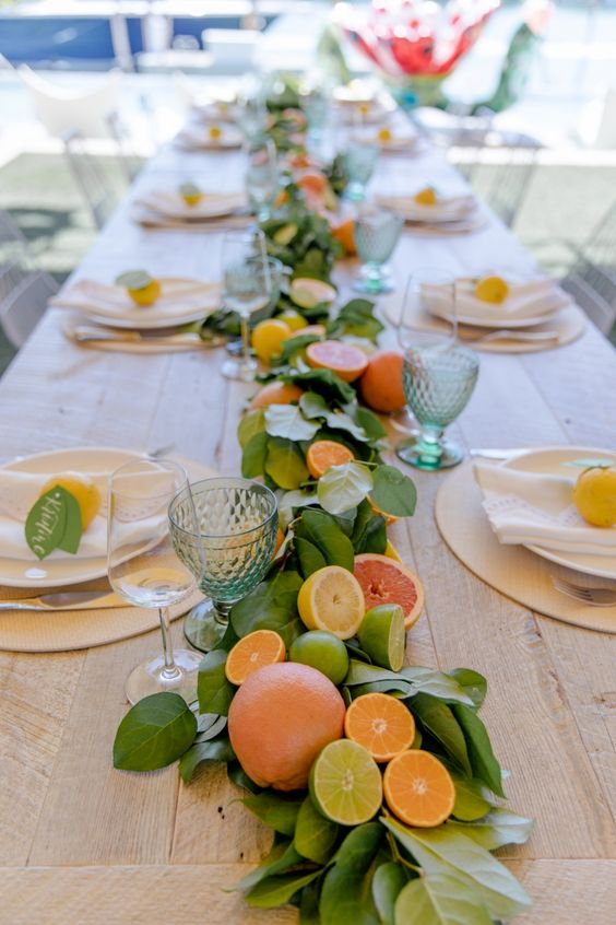 A long table has place settings with lemons on top of plates and a citrus centerpiece runs the length of the table.