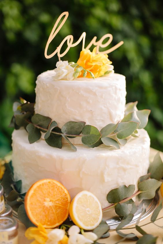 A two-tiered cake with lemon and orange citrus fruit cut in half at the bottom.