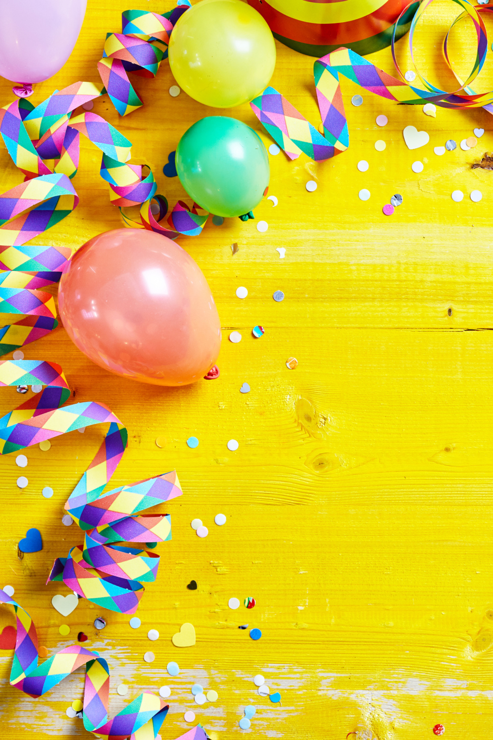 Multi-colored balloons and curled streamers sit atop a bright yellow wooden background.